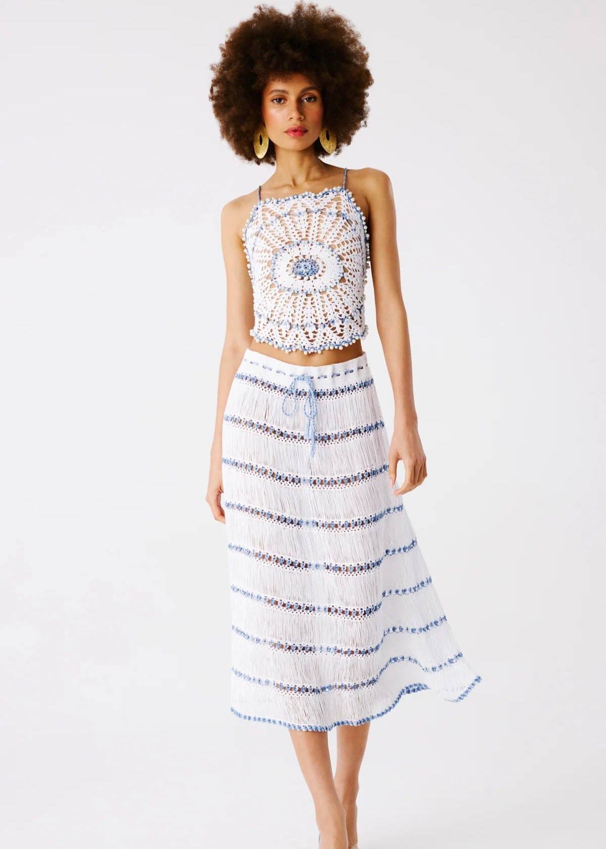 Model wearing white hand-crocheted top and midi skirt featuring pearls and blue accents