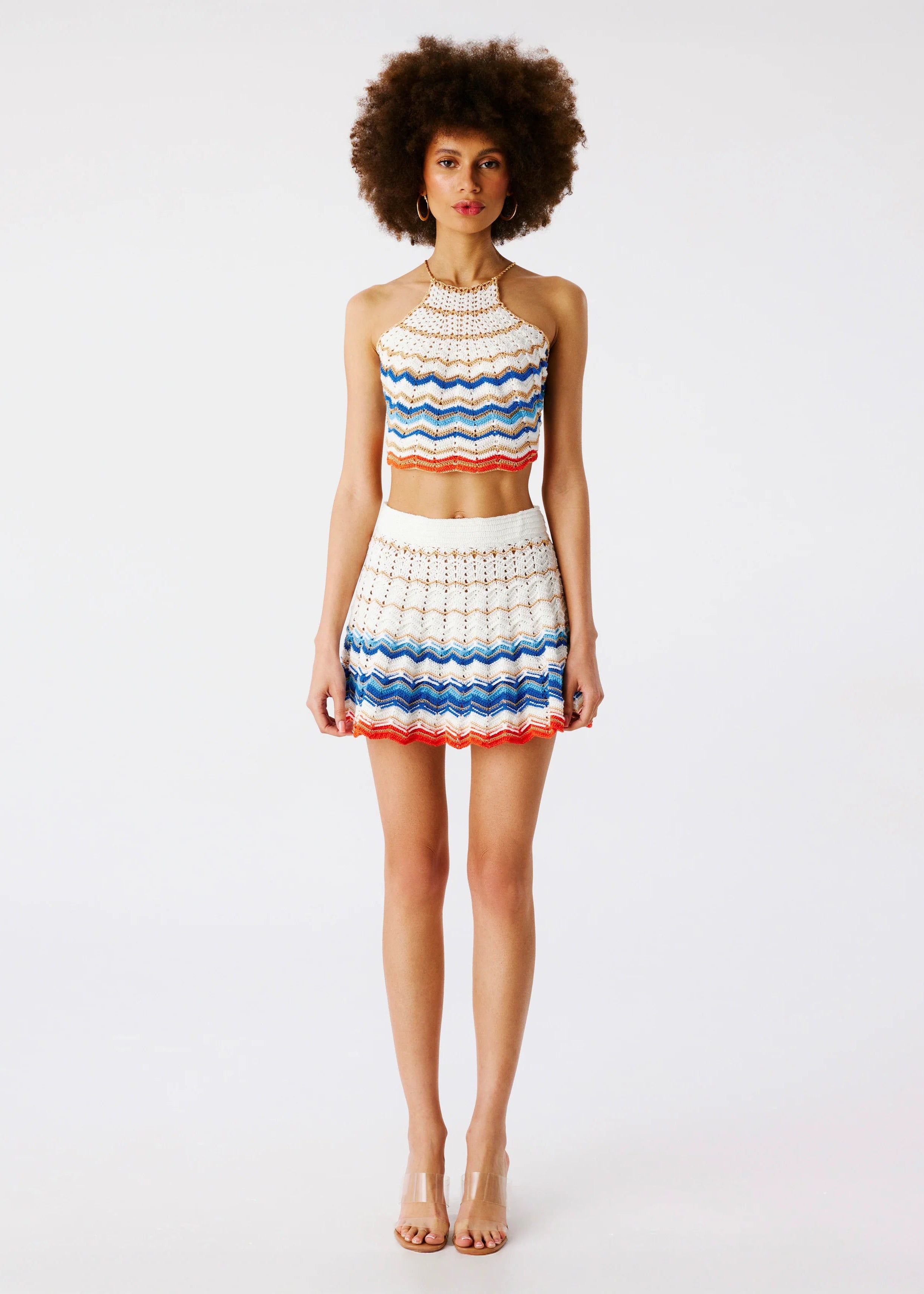 Model wearing matching crocheted mini skirt and halter top featuring zigzag stripes in blue, soft ecru and red