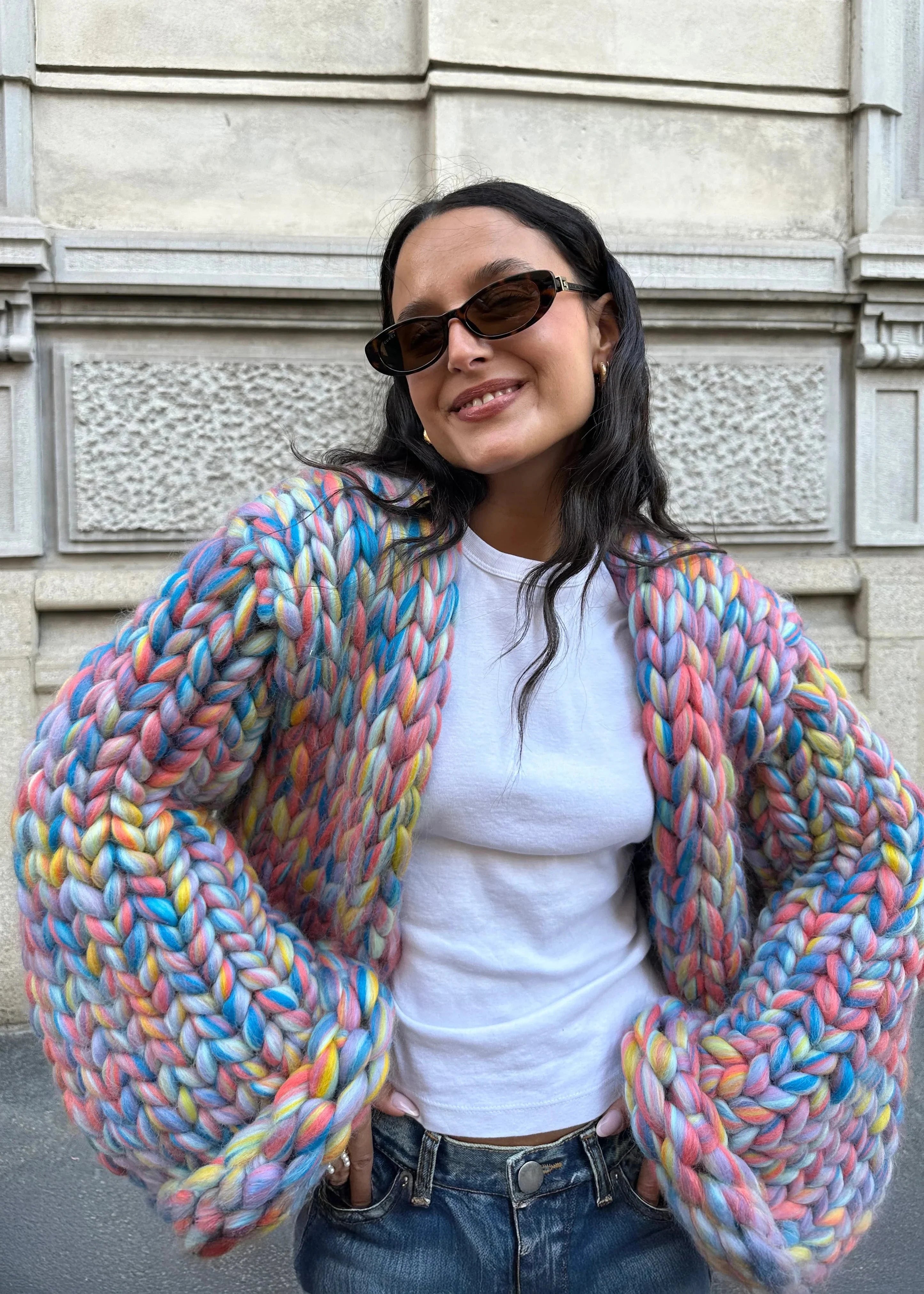 Model wearing a colorful knitted cardigan in front of a building